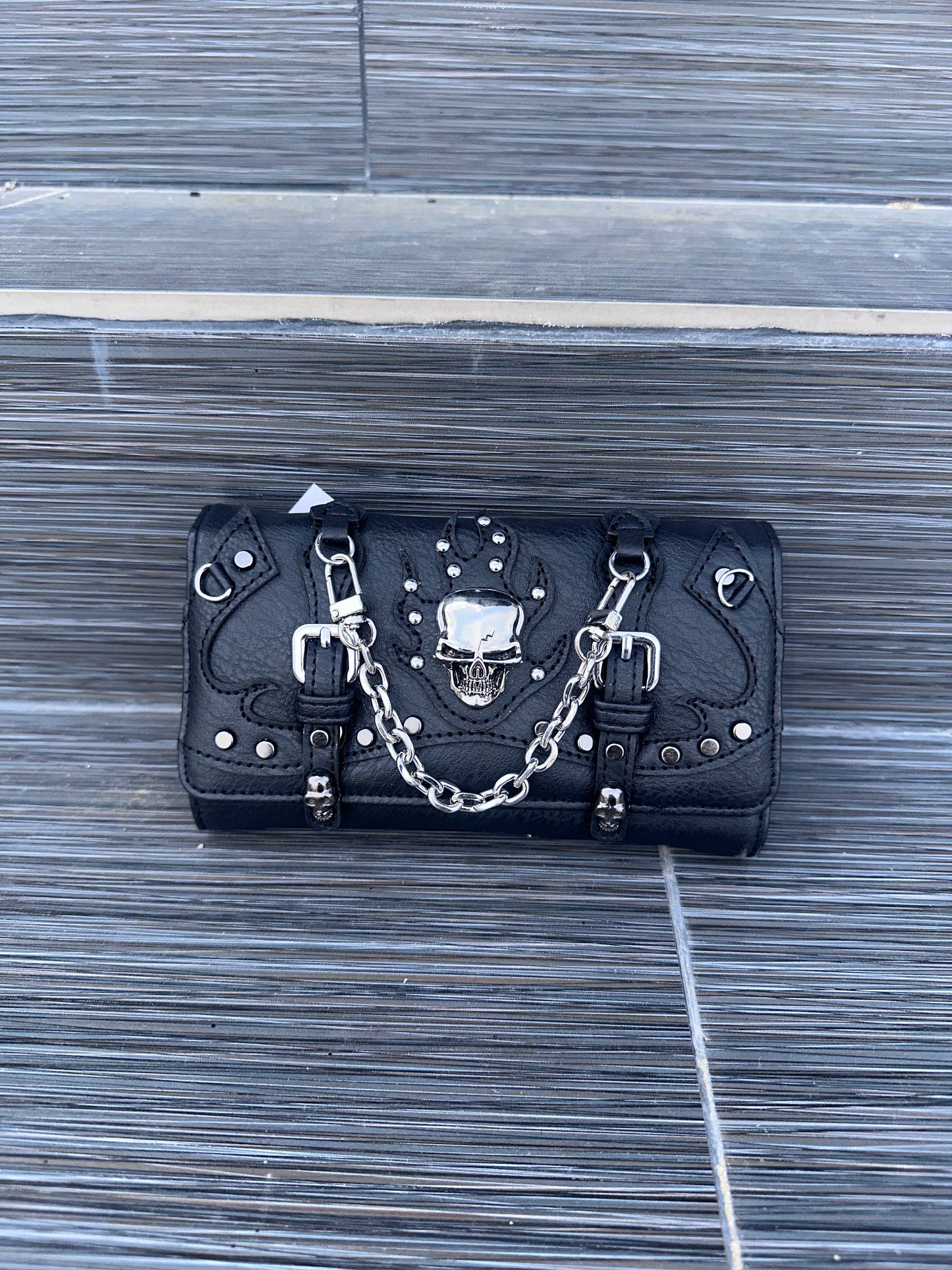 Black leather wallet with skull design and chain on a wooden surface