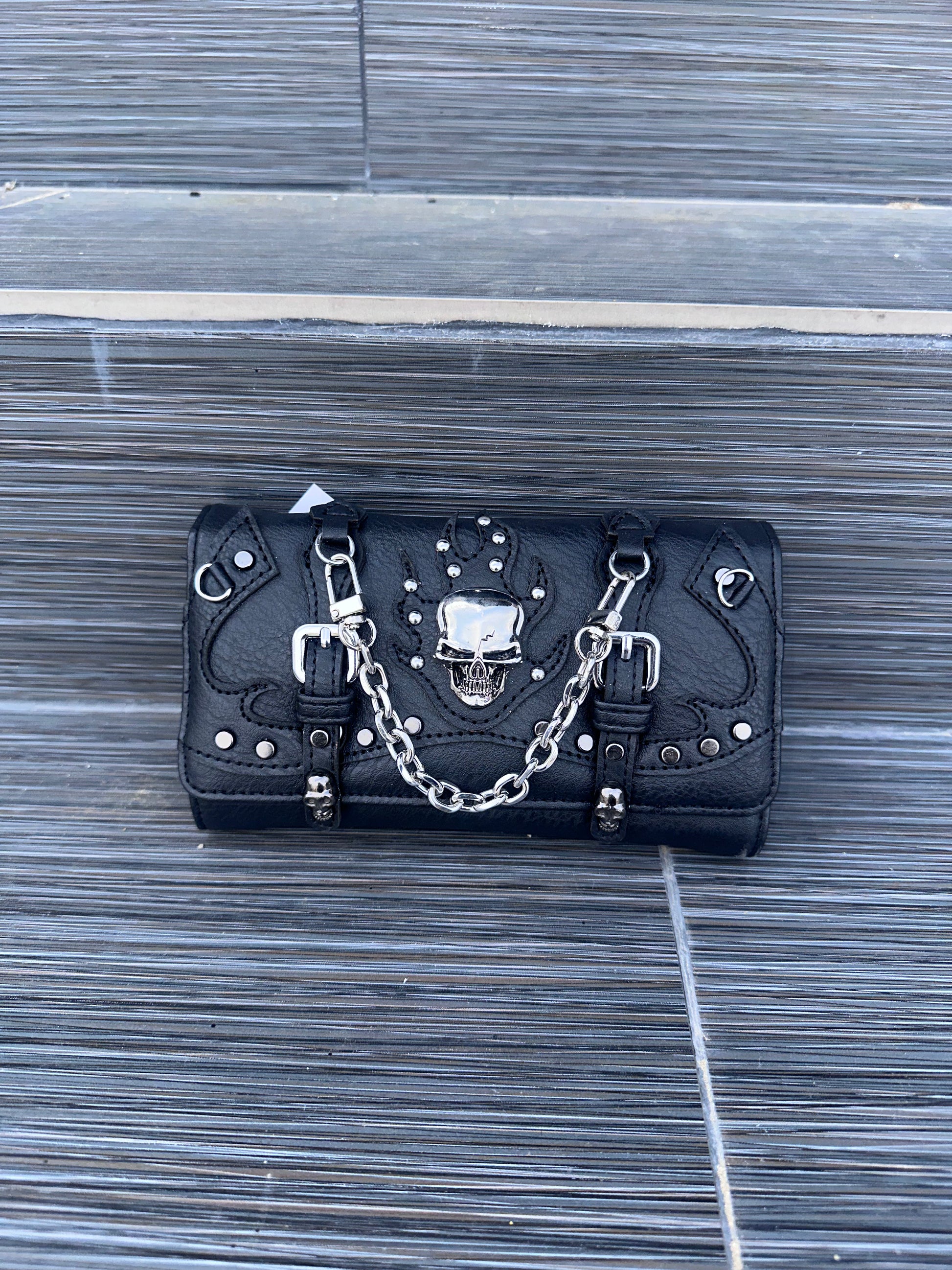 Black leather wallet with skull design and chain on a wooden surface