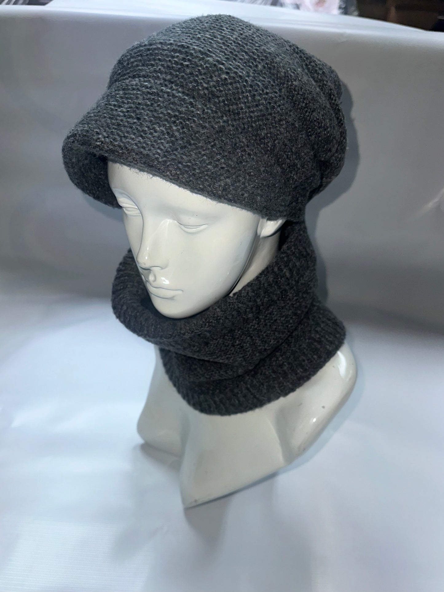 Mannequin head wearing a gray knit hat and scarf on a white background