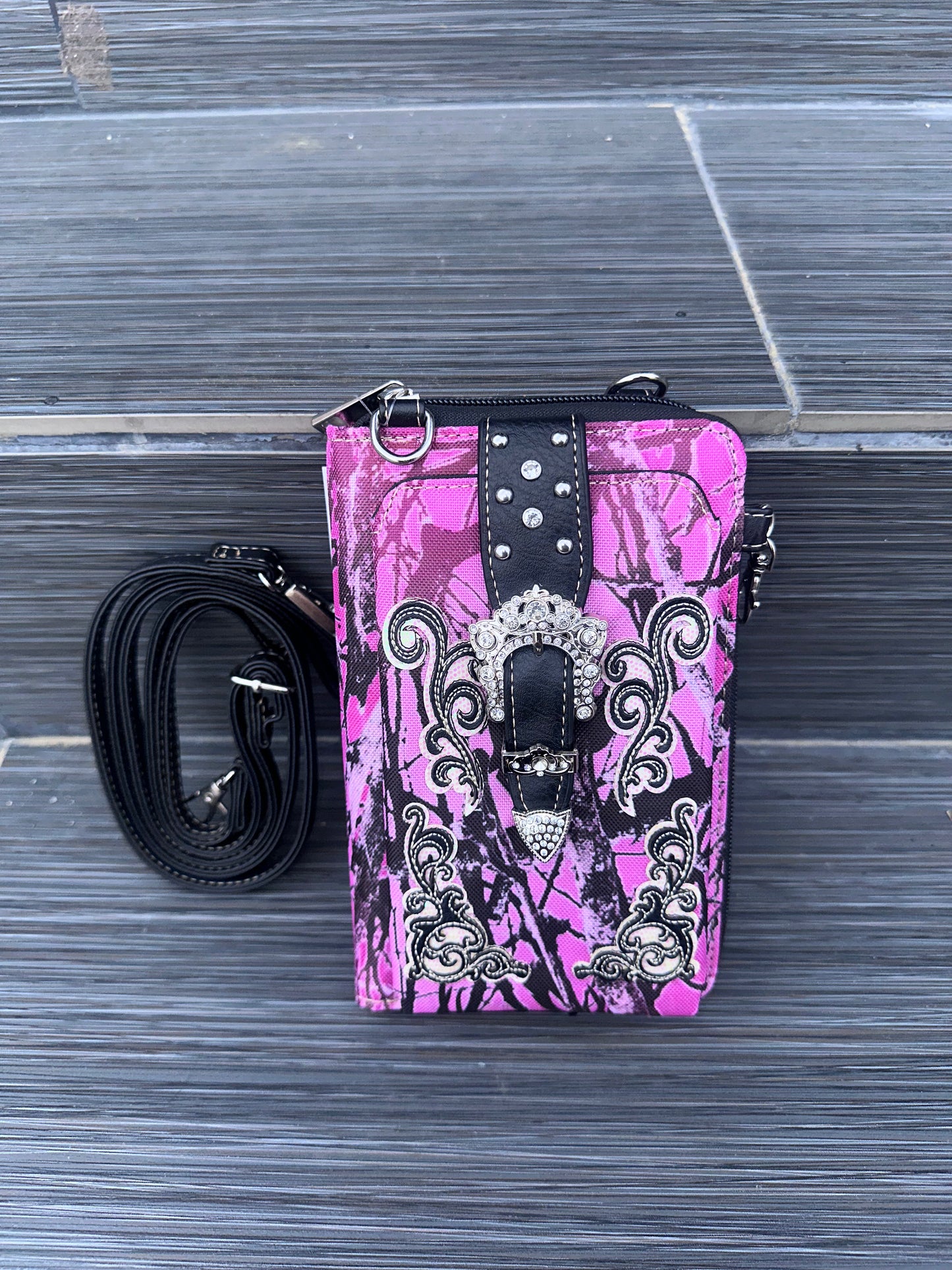 Pink camouflage phone case with black accents and a strap on a gray surface