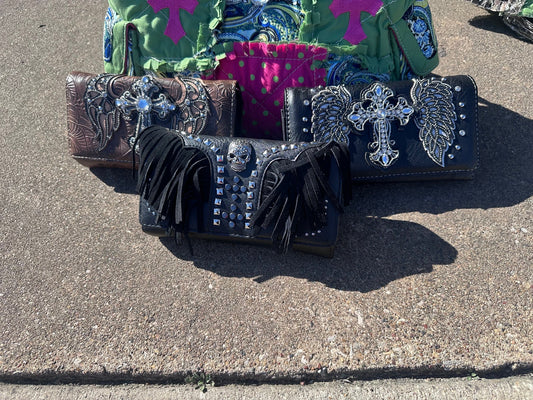 Three wallets with decorative crosses and angel wings on a concrete surface.